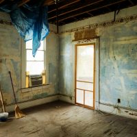 An empty room in an abandoned house with peeling walls and construction tools.
