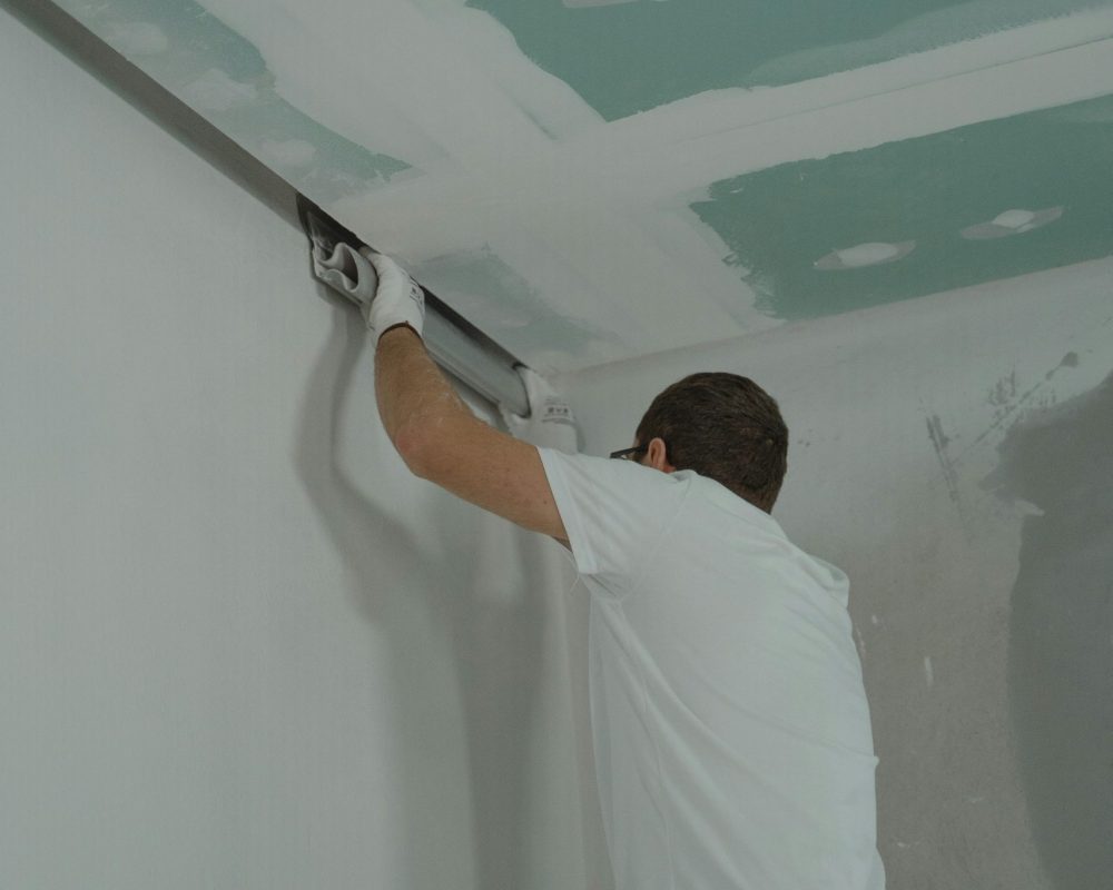 A man works meticulously on drywall installation during a house renovation.