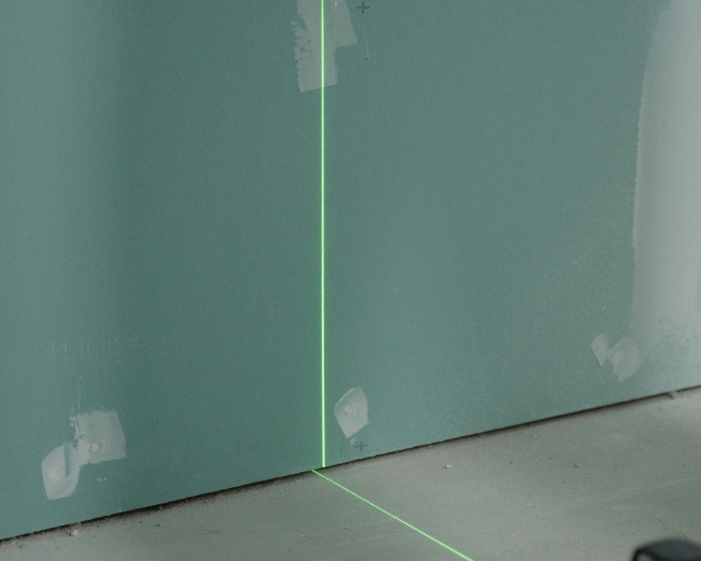 Laser alignment tool projecting light on a wall for precise measurement in construction.